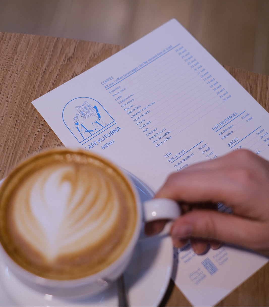 Cappuccino with latte art on a saucer next to a menu on a wooden table.